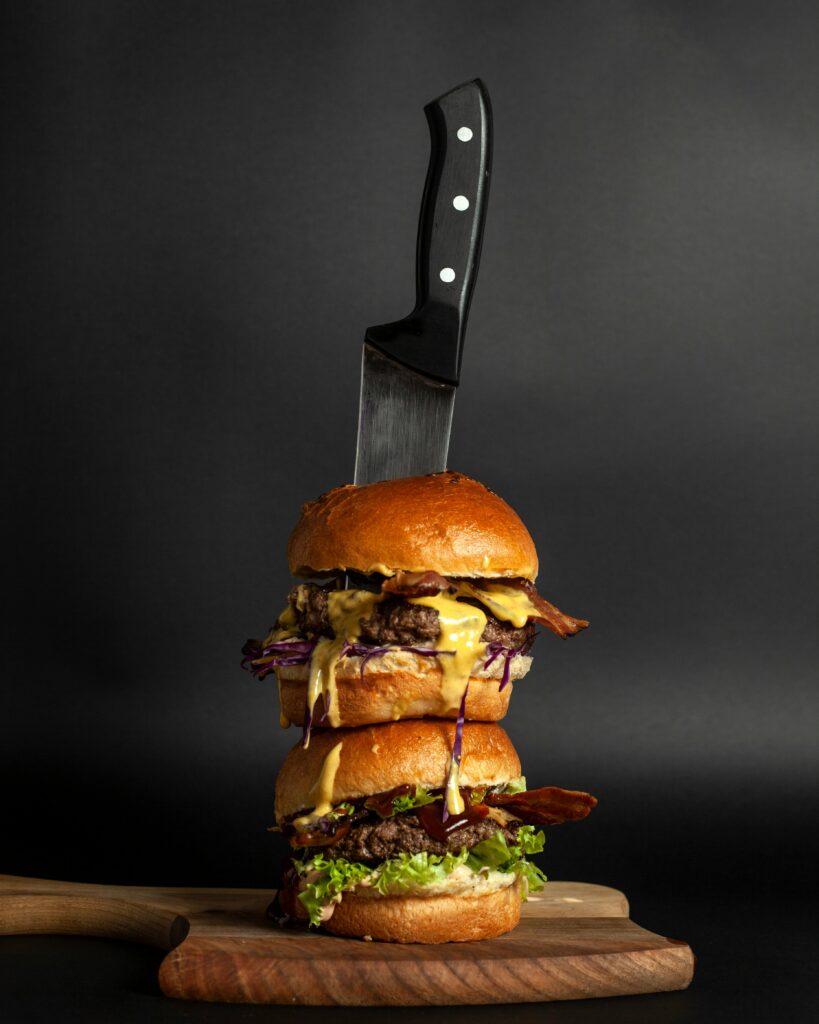 Vertical shot of a double cheeseburger stacked on a wooden board with a knife, perfect for gourmet food themes.