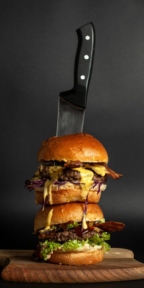 Vertical shot of a double cheeseburger stacked on a wooden board with a knife, perfect for gourmet food themes.